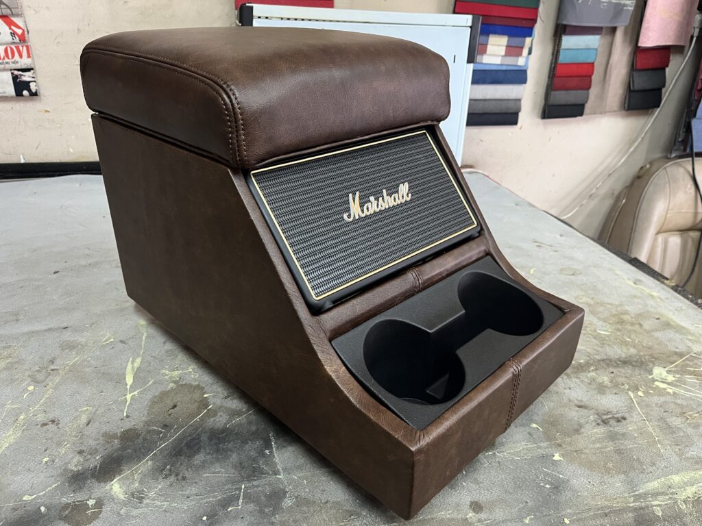Brown leather cubby box with a built-in Marshall speaker and cupholders, made for the Ninety