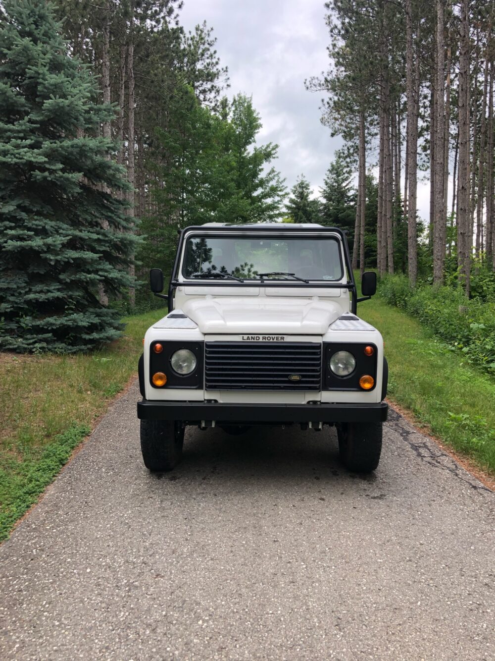 Front view of The NAS, a white 1995 North American Spec Land Rover Defender 90 V8, on a gravel driveway