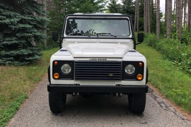 Front view of The NAS, a white 1995 North American Spec Land Rover Defender 90 V8, on a gravel driveway