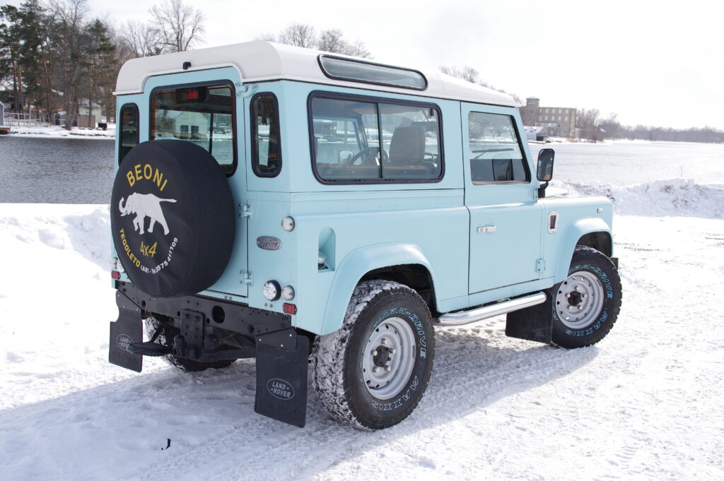 Rear three-quarter view of Blue Crush showing the spare wheel cover and white roof, in the snow
