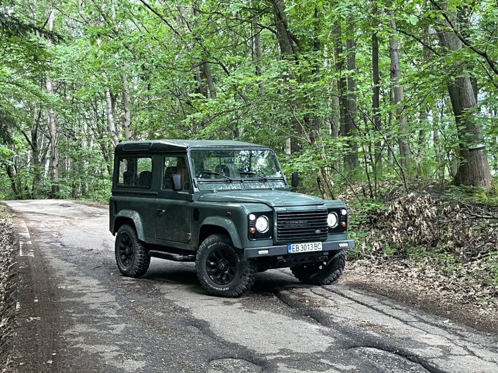 Front three-quarter view of The Evergreen, a Keswick Green Defender 90 with gloss black Sawtooth wheels, in the woods