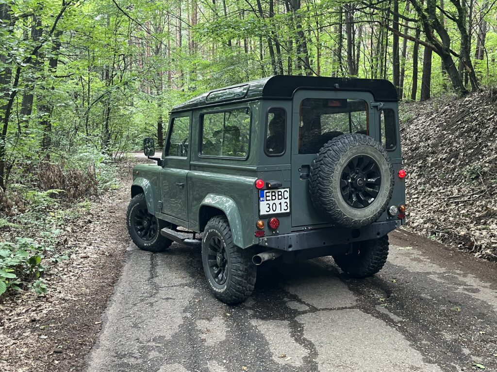 Rear three-quarter view of The Evergreen showing the spare wheel and black roof, on a wooded road