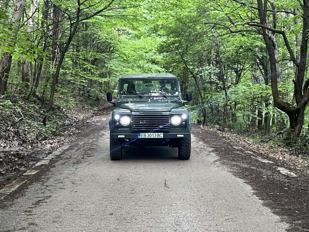 Front view of The Evergreen, a Keswick Green Land Rover Defender 90 Td5 with a black roof, on a forest road