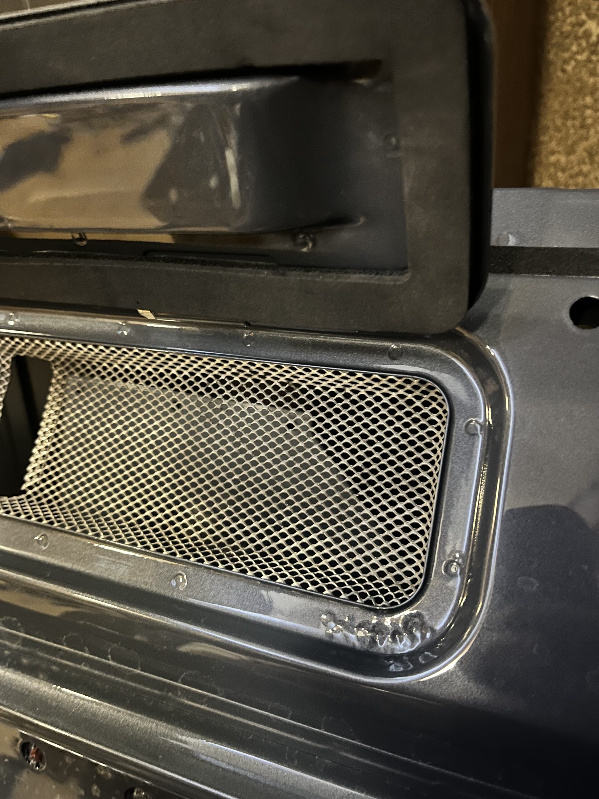 Natural aluminium bulkhead vent mesh riveted back in after paint, against the Ninety's Polymetal Grey